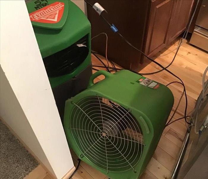 Closeup of an axial air mover and an LGR large dehumidifier drying out a kitchen with the wooden floor visible